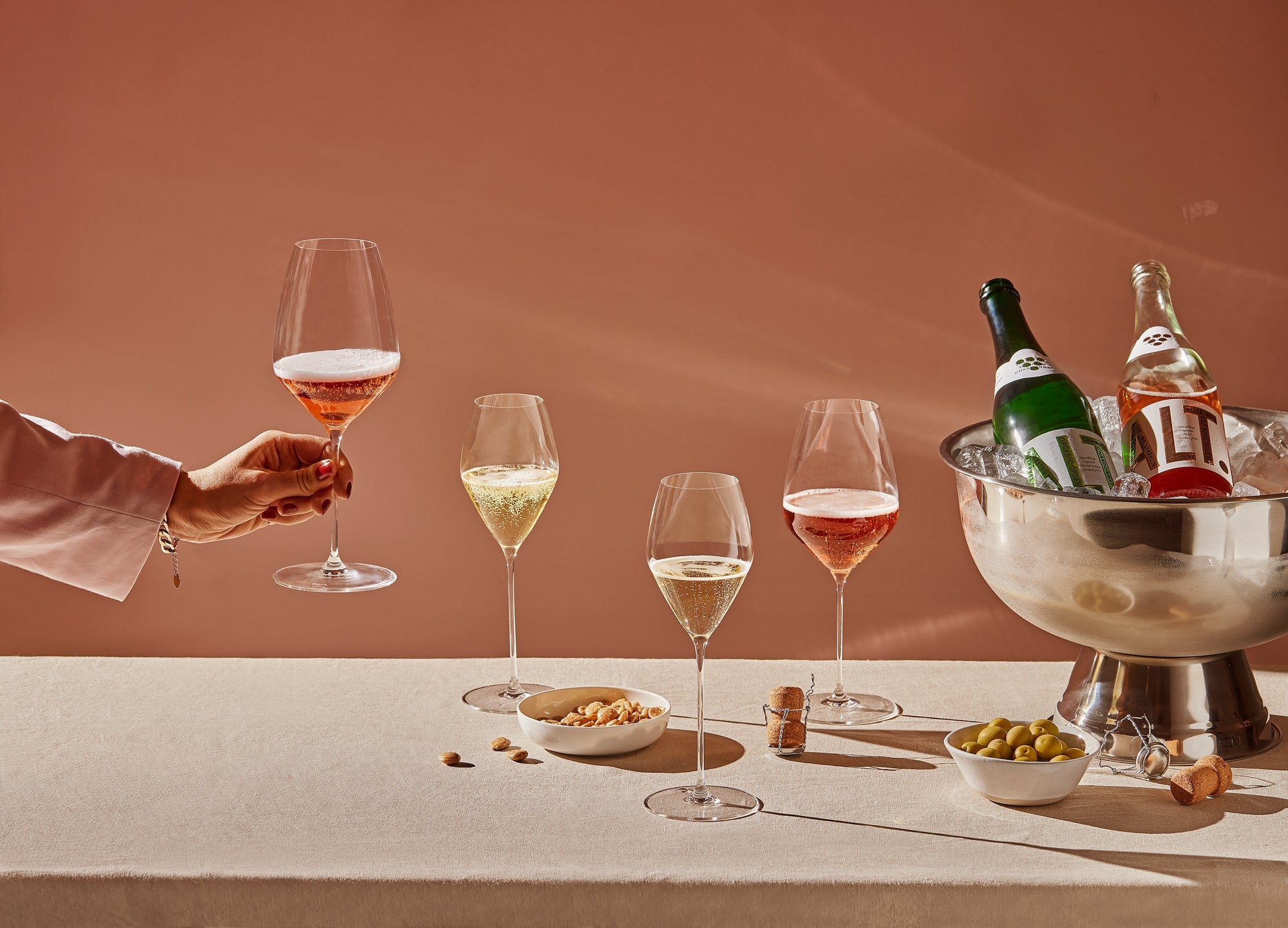 Bilde av ALT. i vinkjøler, fylte glass, snacks og en hånd som tar ett av glassene.